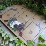 Tarot spread board with a cat skull surrounded by flowers and Ivy leaves, engraved wood